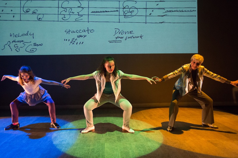 Brenda Bufalino dancing with two other young dancers. A large backdrop of a musical score is behind them.